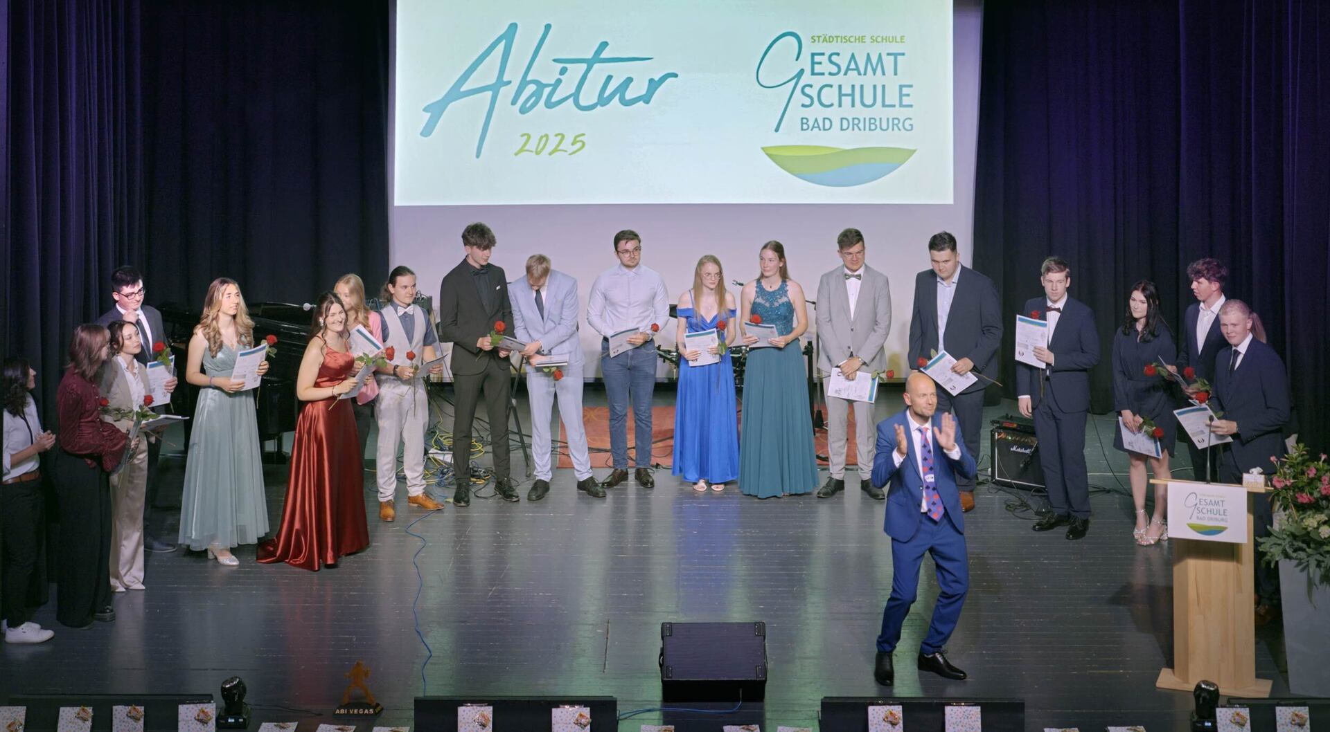 Schülerinnen und Schüler stehen zusammen mit Lehrpersonal auf der Bühne bei der Zeugnisübergabe für das Abitur