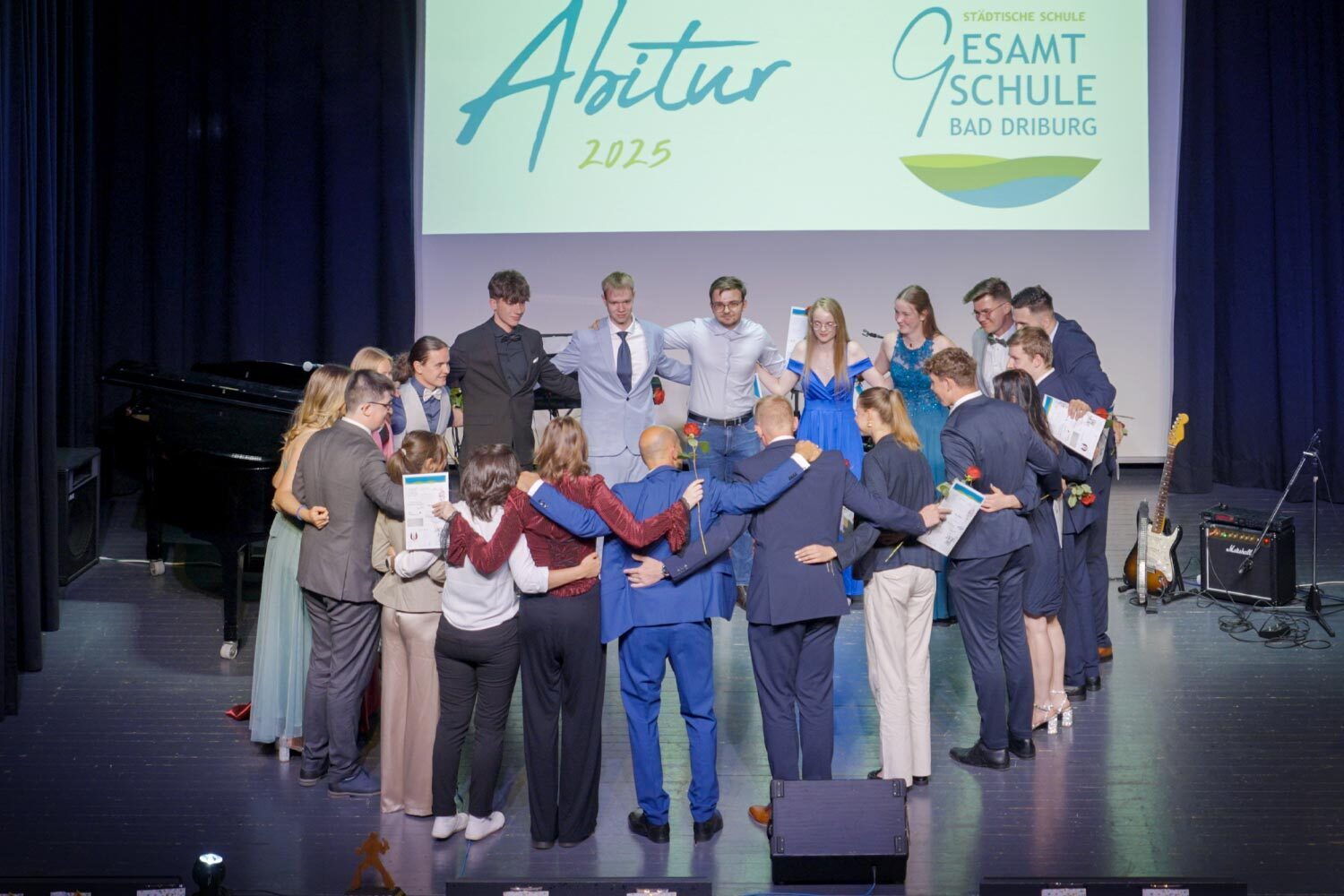Schülerinnen und Schüler stehen zusammen mit Lehrpersonal auf der Bühne bei der Zeugnisübergabe für das Abitur