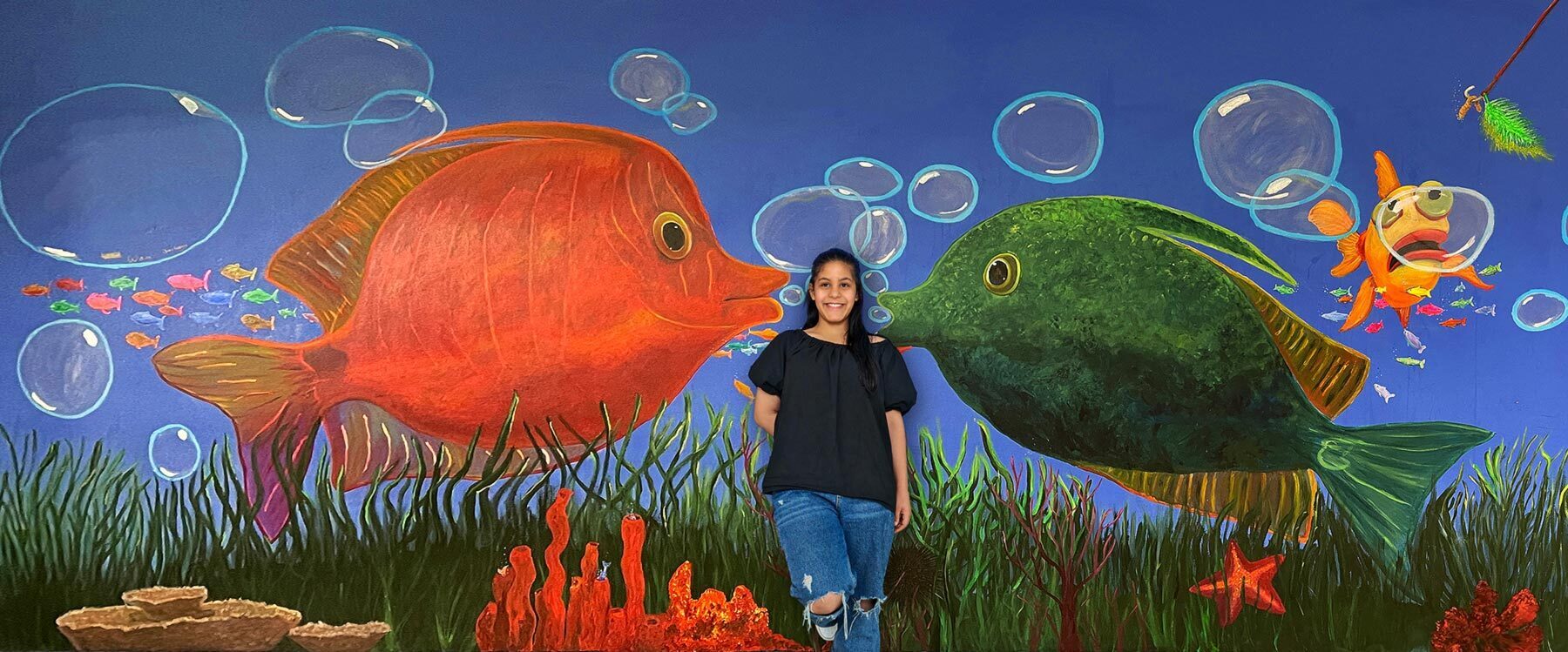 Eine Schülerin steht vor einem Wandgemälde der Schule