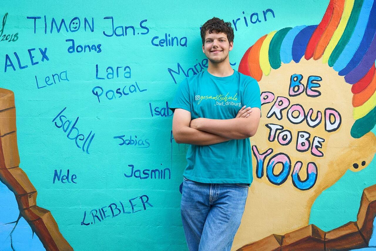 Ein Oberstufenschüler steht vor einem Wandgraffiti der Schule