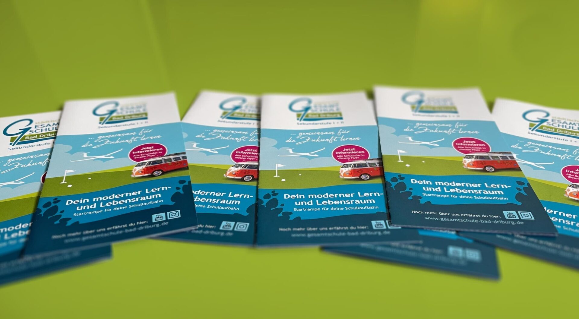 Mehrere Exemplare des Schulflyers liegen auf einer grünen Fläche verteilt