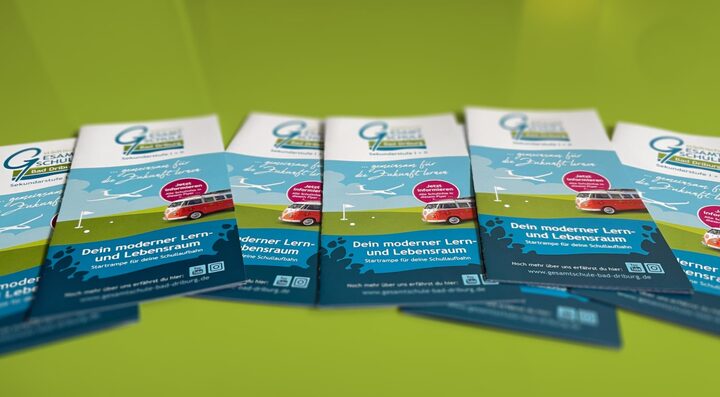 Mehrere Exemplare des Schulflyers liegen auf einer grünen Fläche verteilt