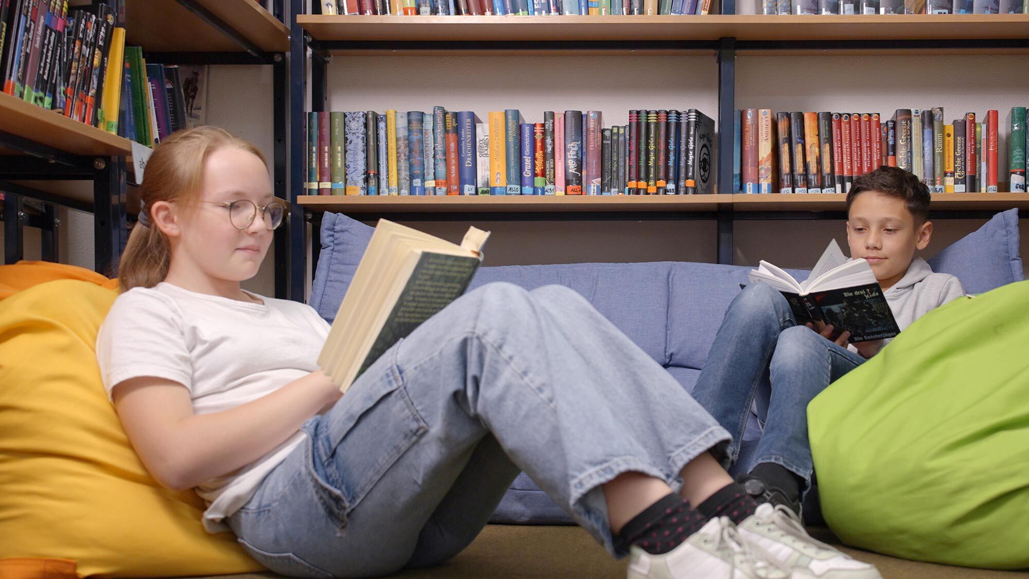 Eine Schülerin und ein Schüler sitzen in Sitzsäcken in der Schulbibliothek und lesen