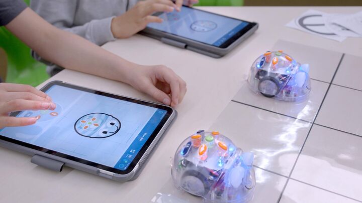Auf dem Tablet ist ein Miniroboter als Zeichnung zu sehen, mit dem der davor stehend Miniroboter gesteuert werden kann