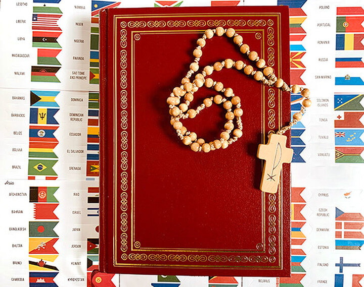 Eine Bibel, eine Kette mit Kreuz daran auf einer Länderflaggen-Übersicht liegend