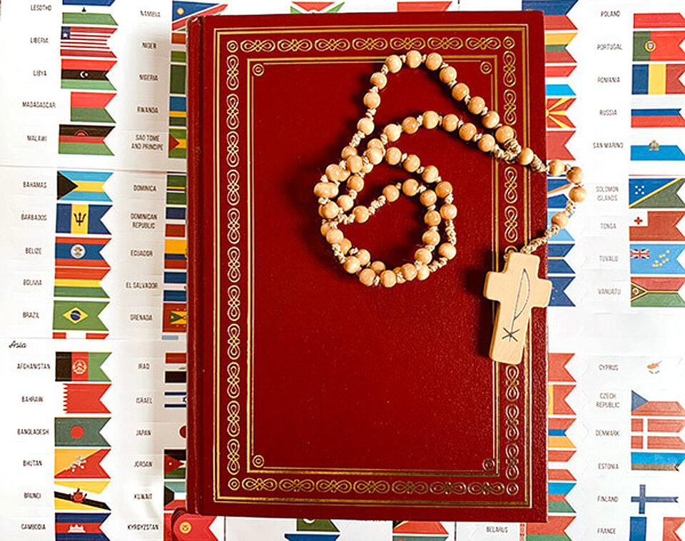 Eine Bibel, eine Kette mit Kreuz daran auf einer Länderflaggen-Übersicht liegend