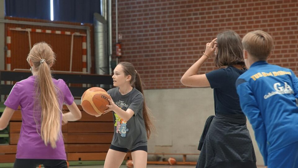 Schülerinnen und ein Schüler spielen Basketball