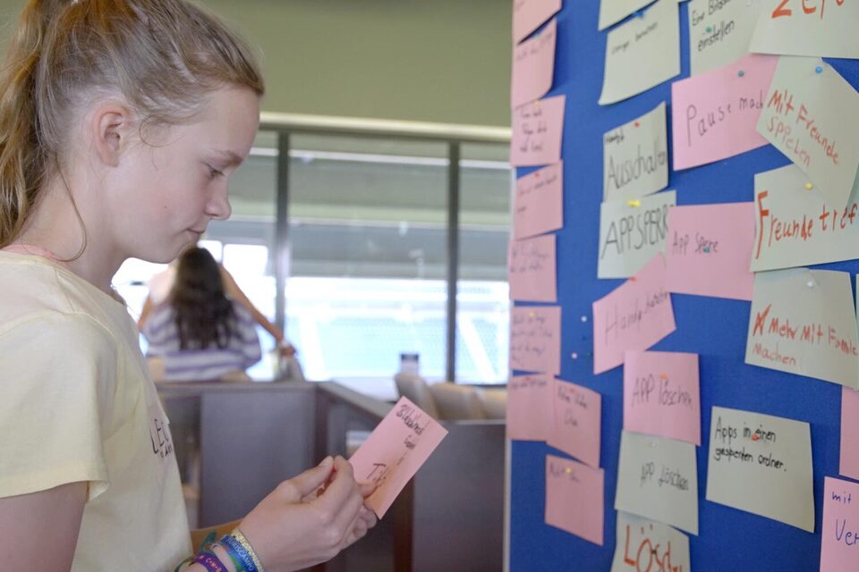 Kind steht vor einer Tafel, an der Zettel hängen auf denen Wörter geschrieben sind