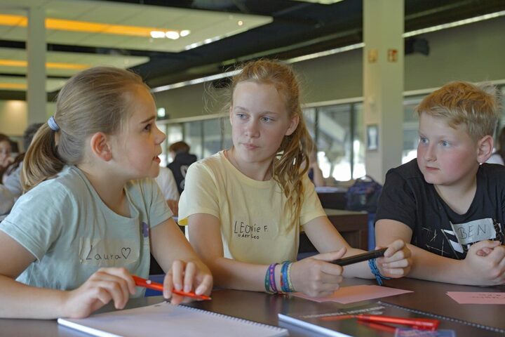 Zwei Schülerinnen und ein Schüler sitzen zusammen am Tisch und unterhalten sich