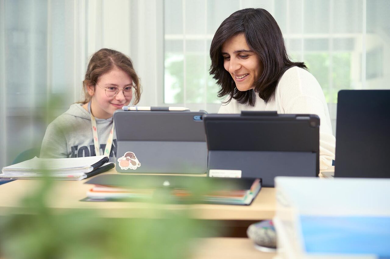 Eine Lehrerin erklärt die Funktionsweise eines Tablets einer Schülerin